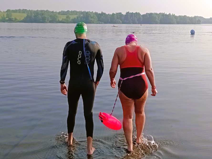 Two swimmers entering the water one in a wetsuit the other in a swim suit